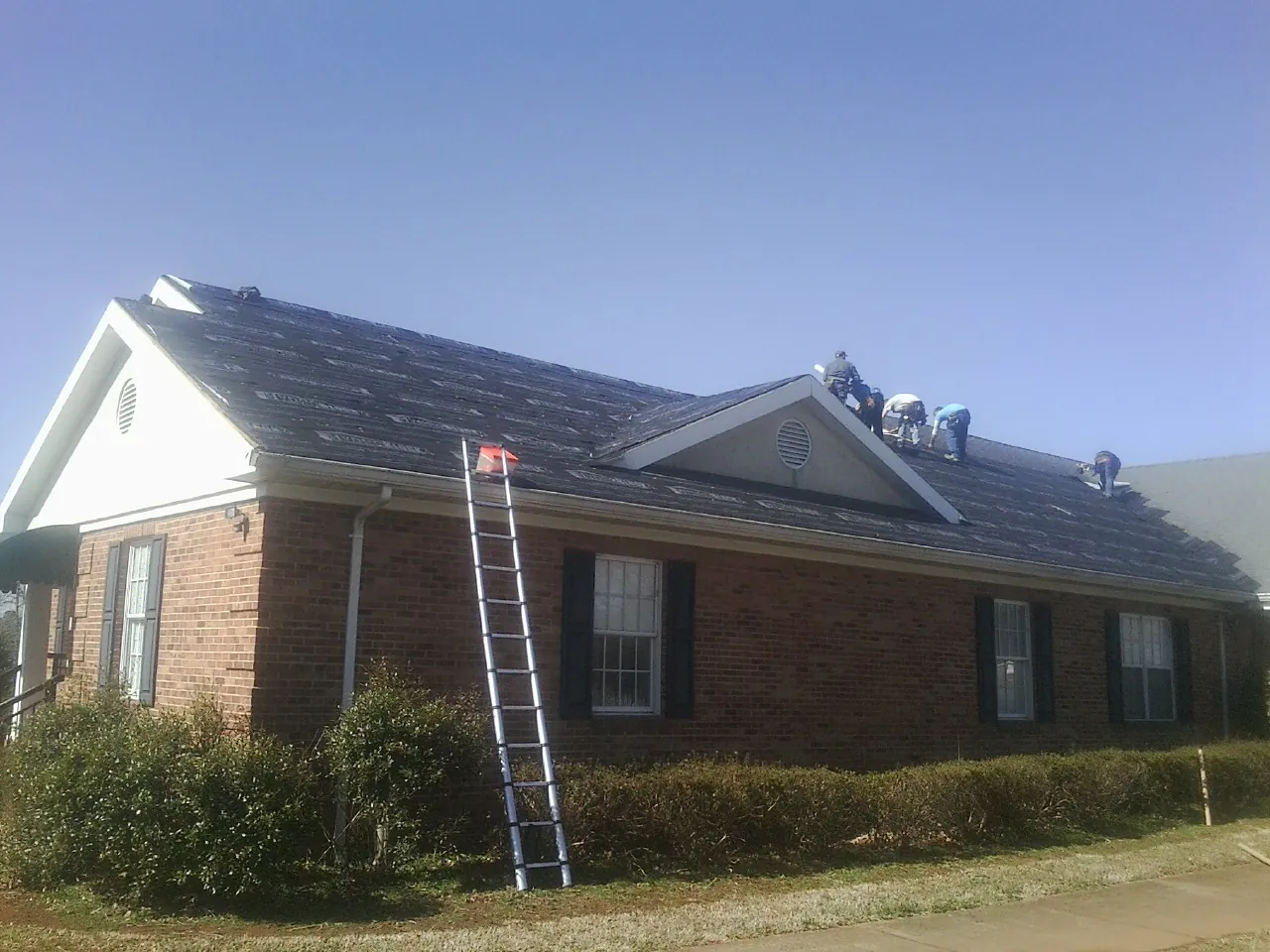 Crew tearing shingles off a brick ranch roof with a ladder set — Emergency Roof Repair work by our crew in Middlebury