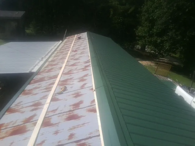 Old rusted panels beside newly installed green metal roofing — Wind Damage Roof Repair by Roofing Brothers in Middlebury