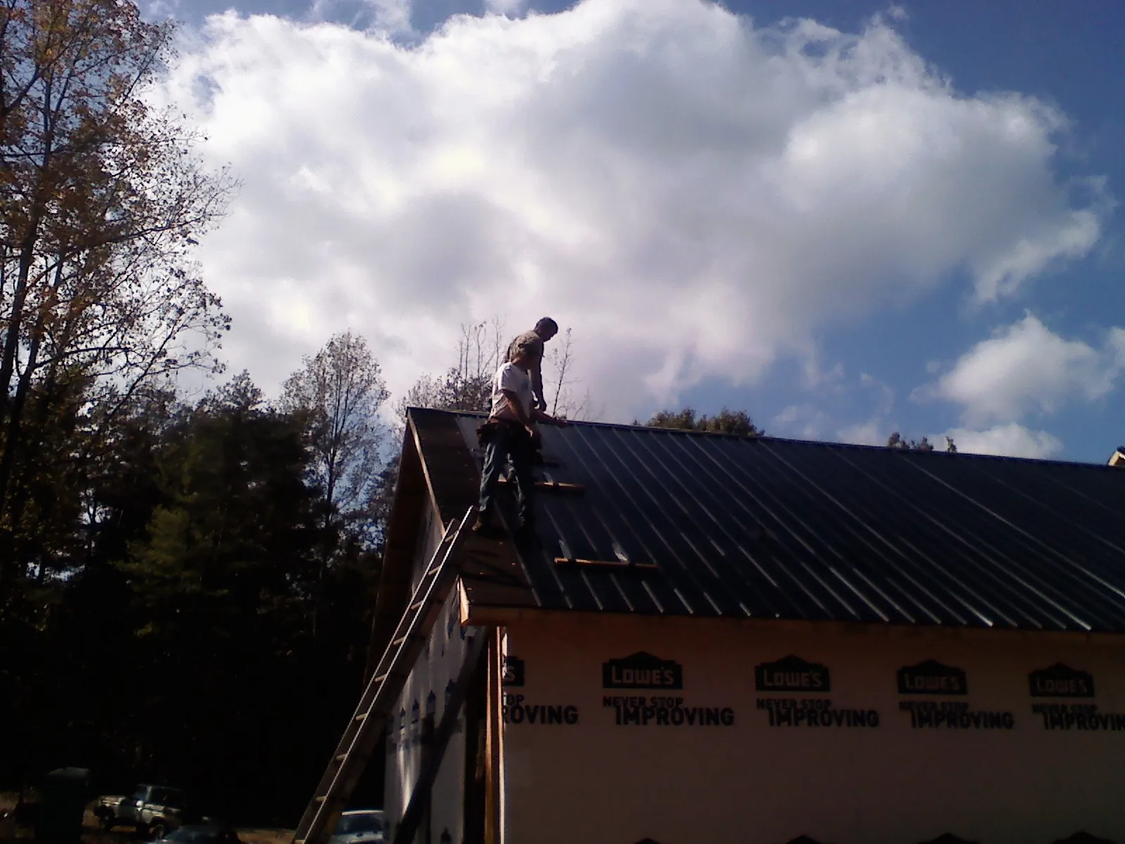 Roofer fastening dark metal panels high against a cloudy sky, from a Roof Inspection job in Middlebury