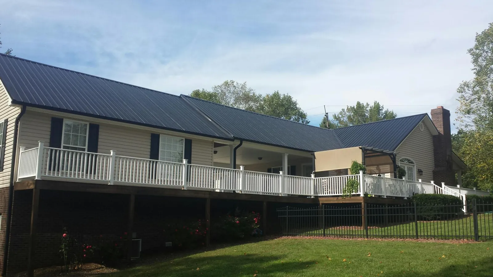 Black metal roof above a long white railed deck on a hillside home in Middlebury